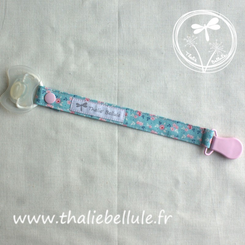 Attache tétine bleu à fleurs roses en tissu coton, avec une pince plastique rose.